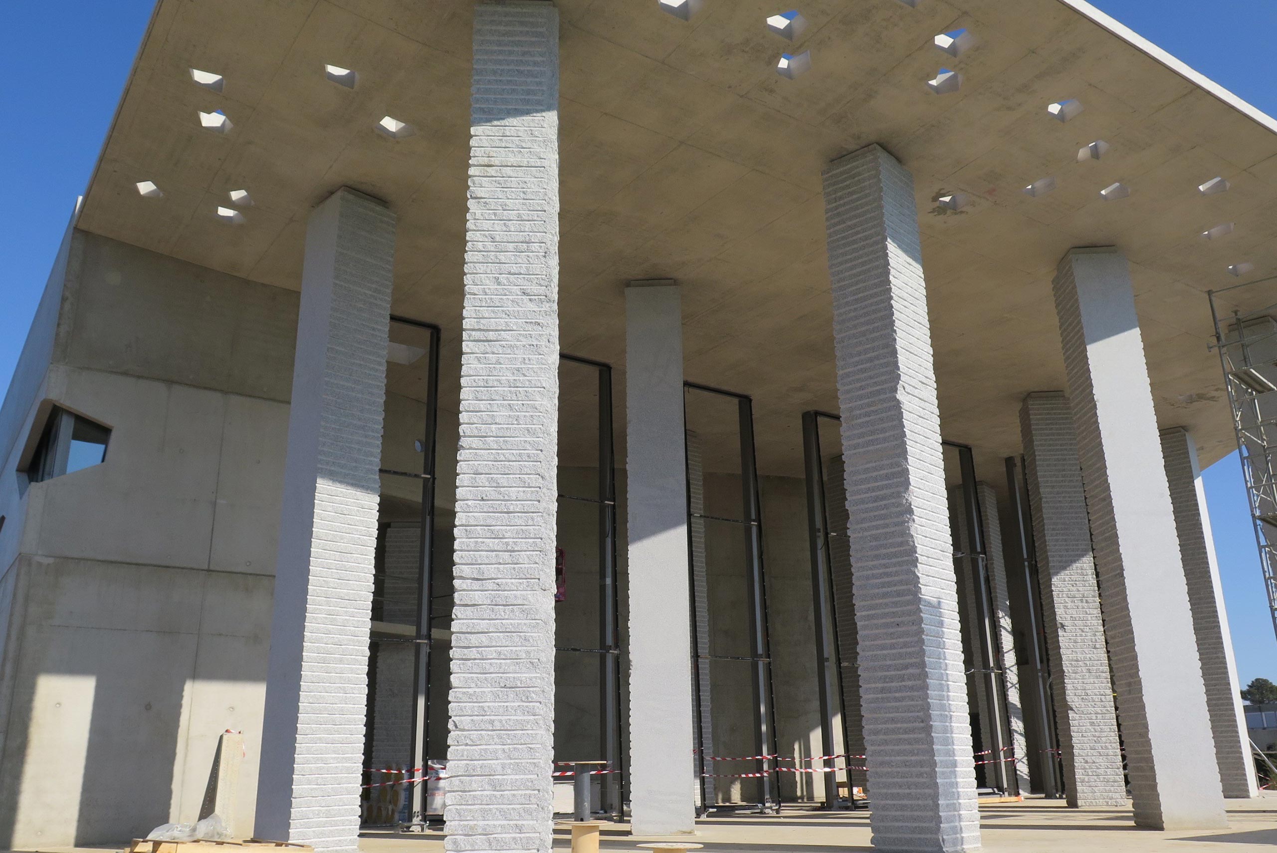 A large concrete hood with scattered cutouts held up by 13 granite support columns covers the courtyard of the future Agora auditorium.  Image: CEMEX France