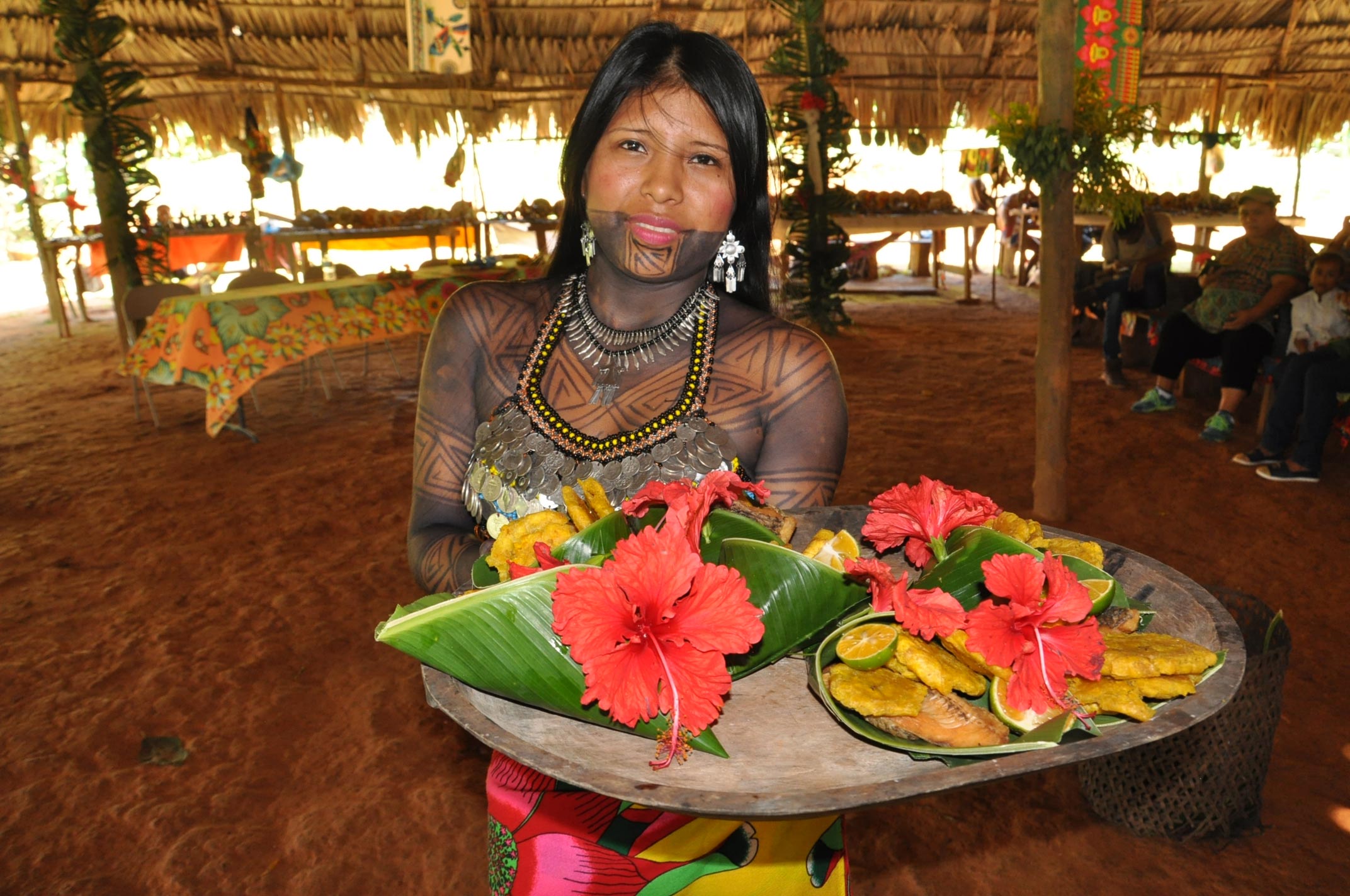 An Emberá woman in traditional garb displays a tray of food decorated with flowers